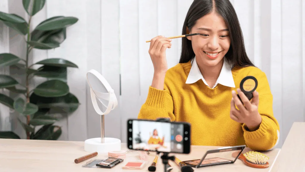 A content creator using her smartphone to film an eye makeup tutorial, representing how micro-creators engage audiences and generate revenue through digital content.
