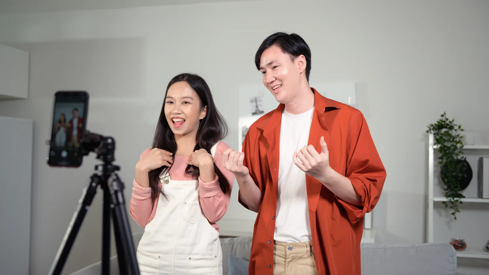 Two young TikTok creators filming a video together at home using a smartphone on a tripod